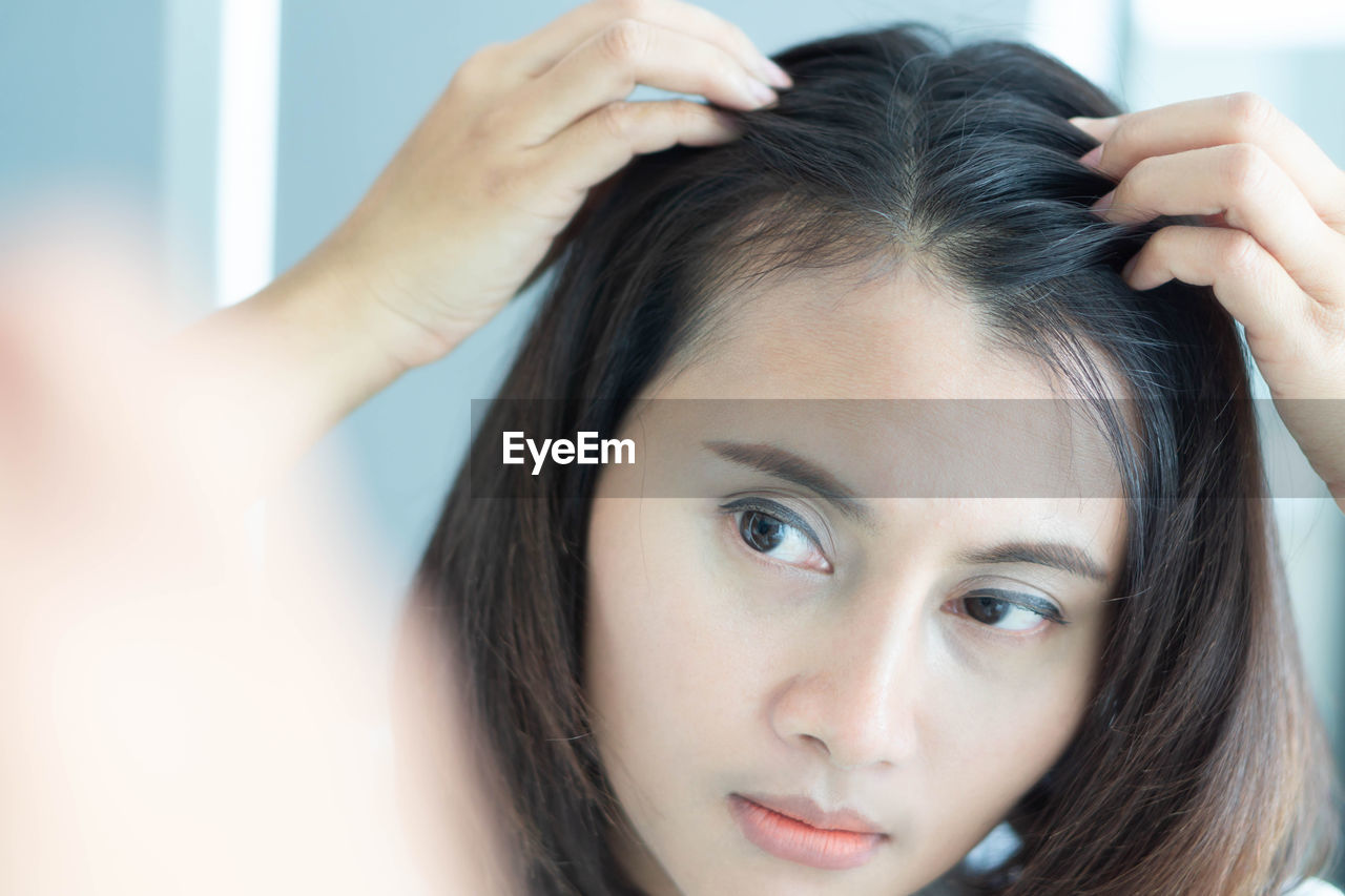 Reflection of woman looking at hair on mirror