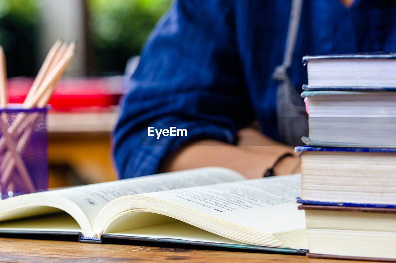 Midsection of person reading with stack of books on table