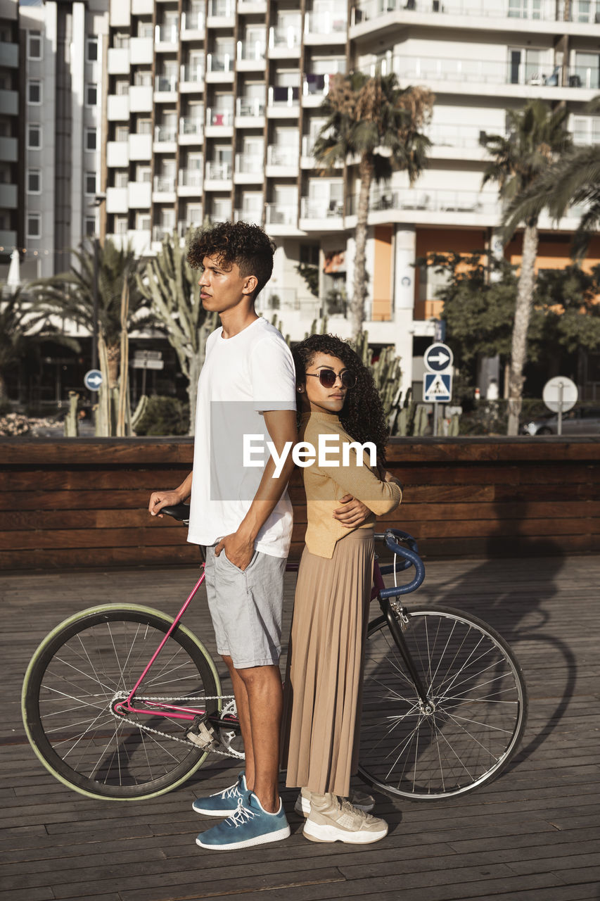 Cool couple with bicycle in the city, standing back to back