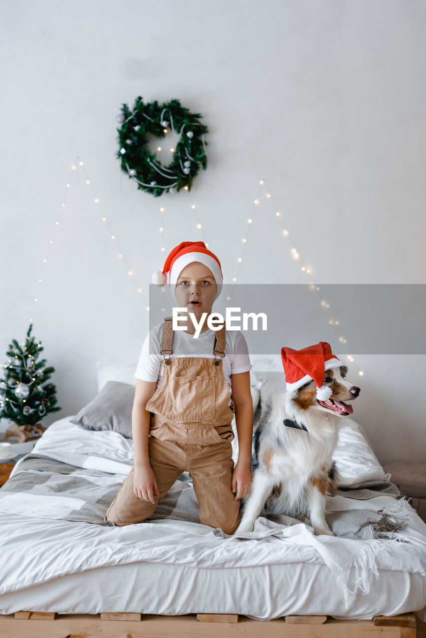 A boy and a dog in red santa hat having fun on bed. best friends. christmas mood. festive atmosphere