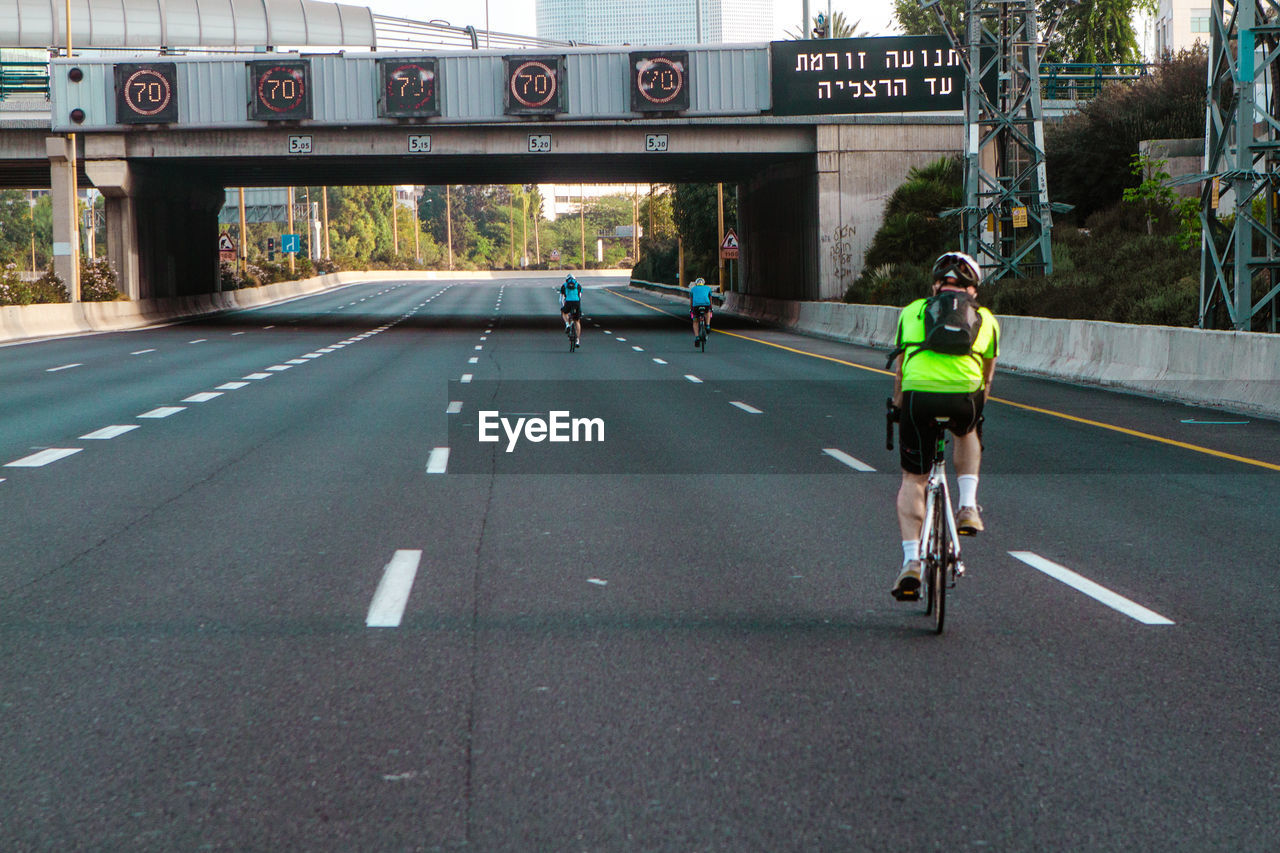 Rear view of man riding bicycle on empty highway. approaching overpass 