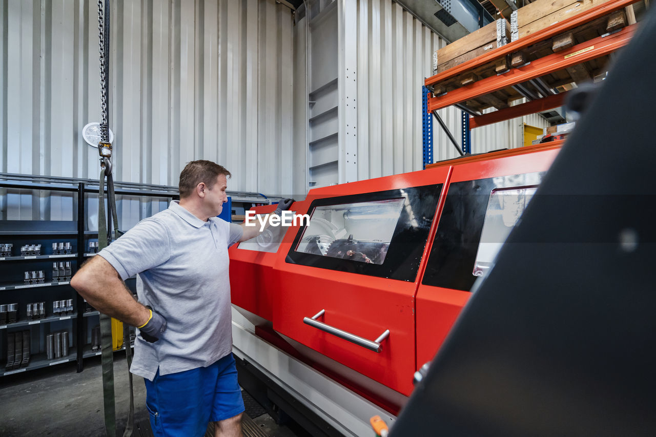 Male manual worker with hand on hip standing by machinery at industry