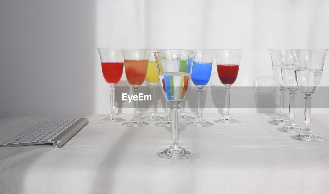 Close-up of wineglasses with keyboard on table against wall