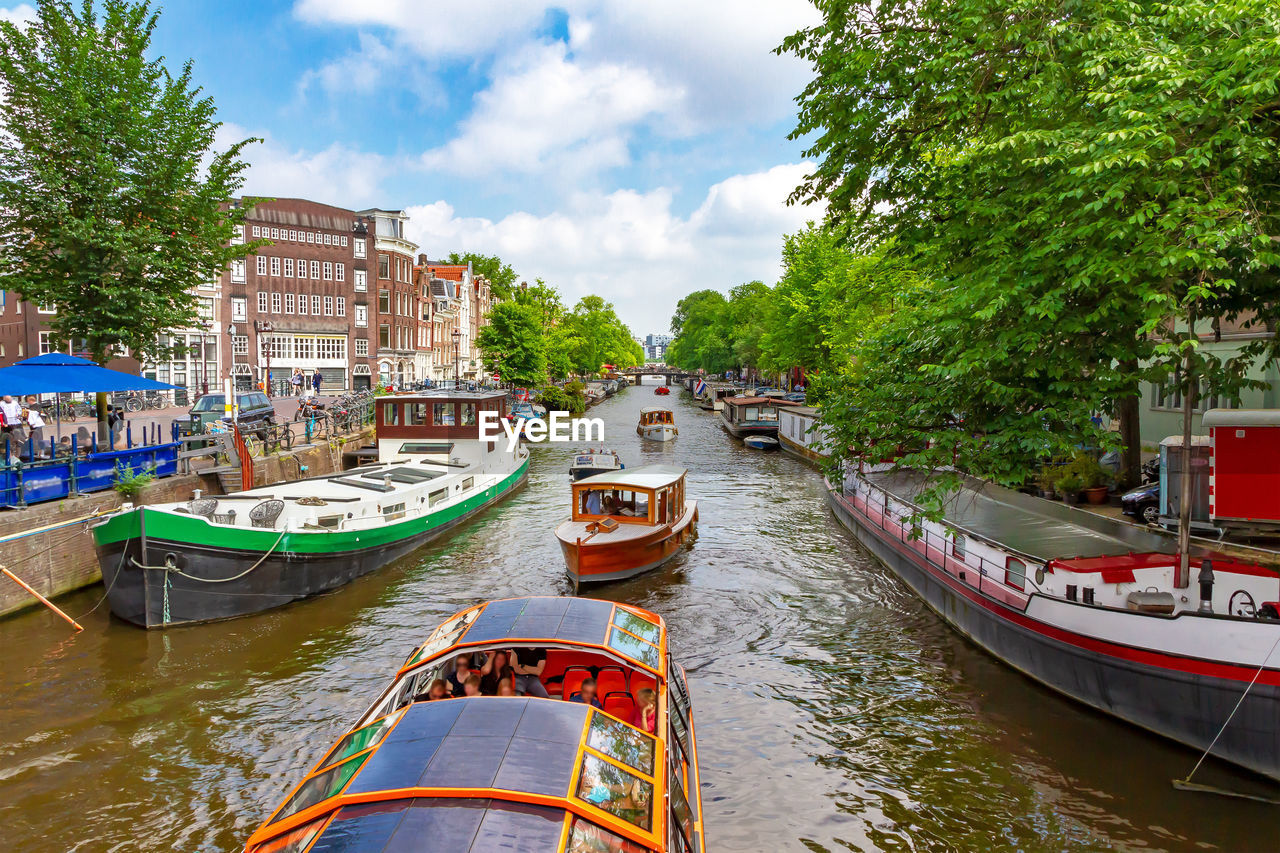 BOATS MOORED IN CANAL AMIDST TREES AGAINST SKY