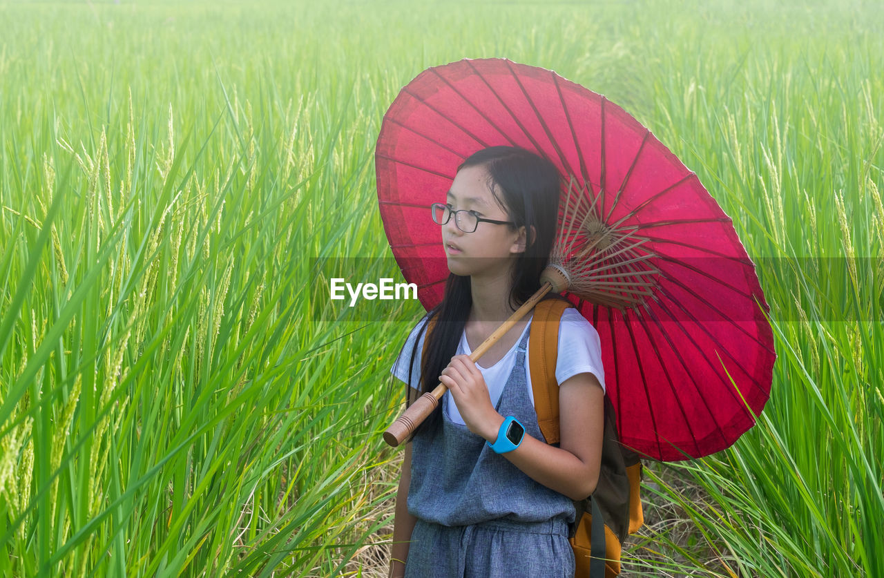 Girl holding red umbrella while standing at farm