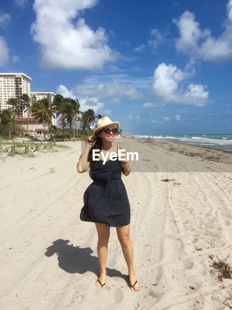 Smiling young woman standing on sandy beach against sky