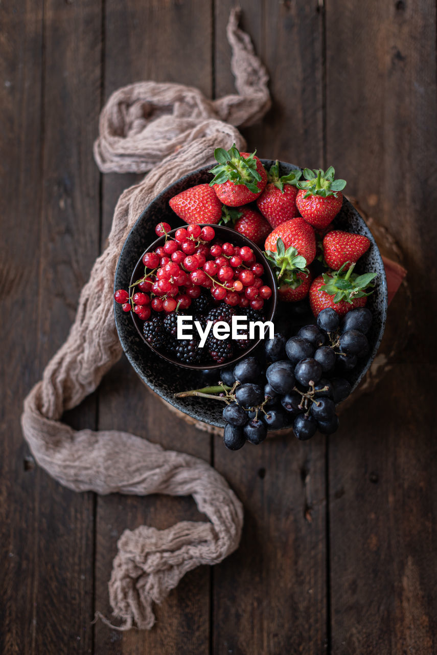 Top view of bowl with various healthy fruits and berries placed on table near old towel in rustic kitchen