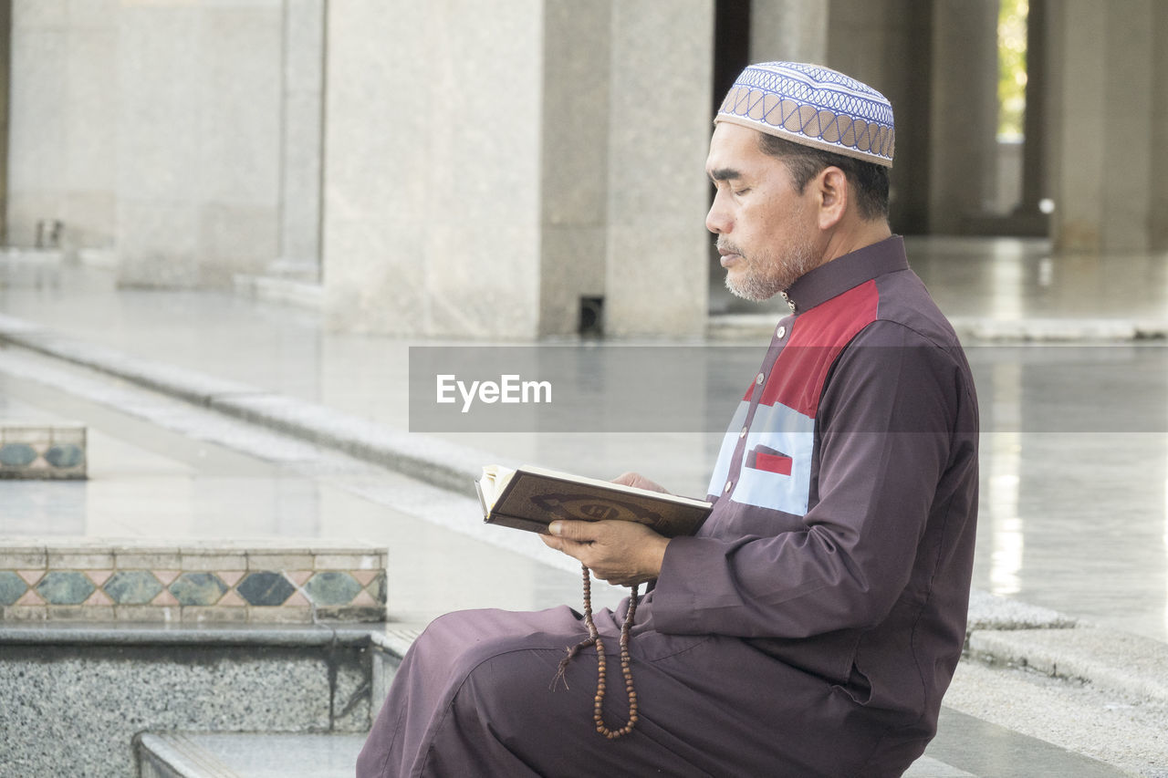 Mature man reading koran while sitting at mosque