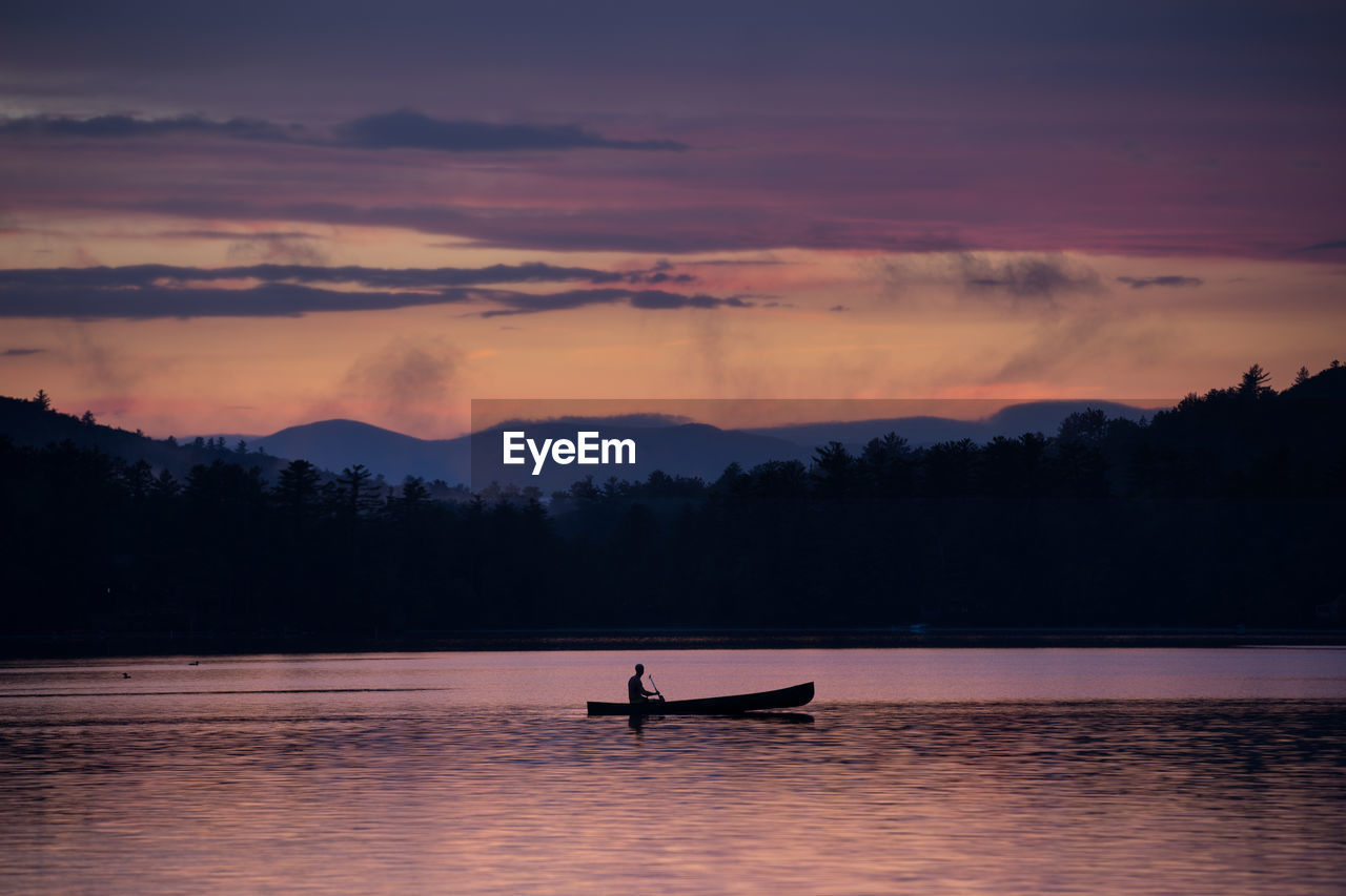 Silhouette person in boat on lake against sky during sunset
