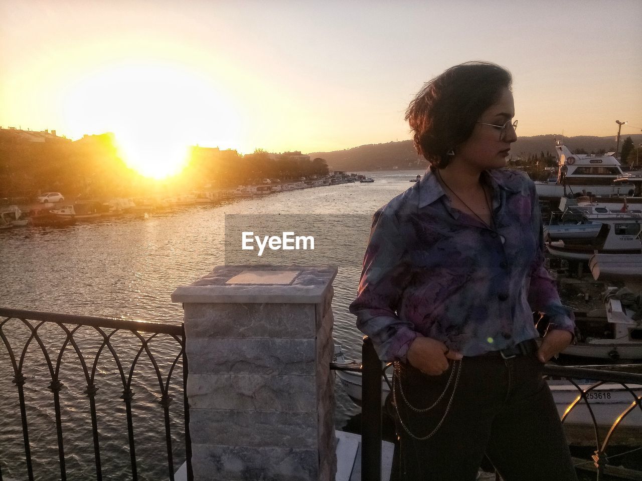 Woman standing by railing against sky during sunset