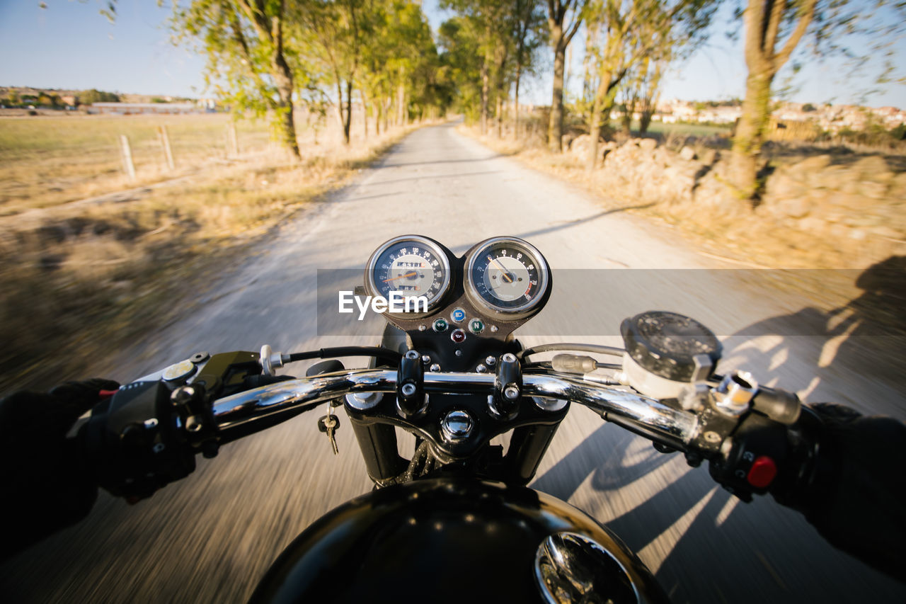 Back view of faceless fast racer riding motorbike through forest in rural location