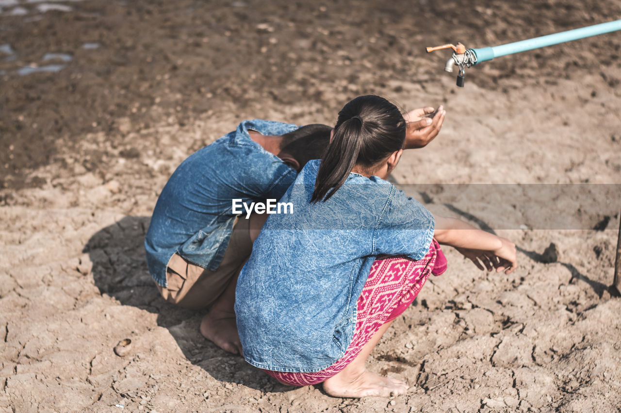 Siblings crouching by tap on drought field