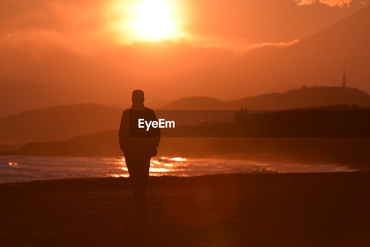 Rear view of a silhouette man overlooking calm lake