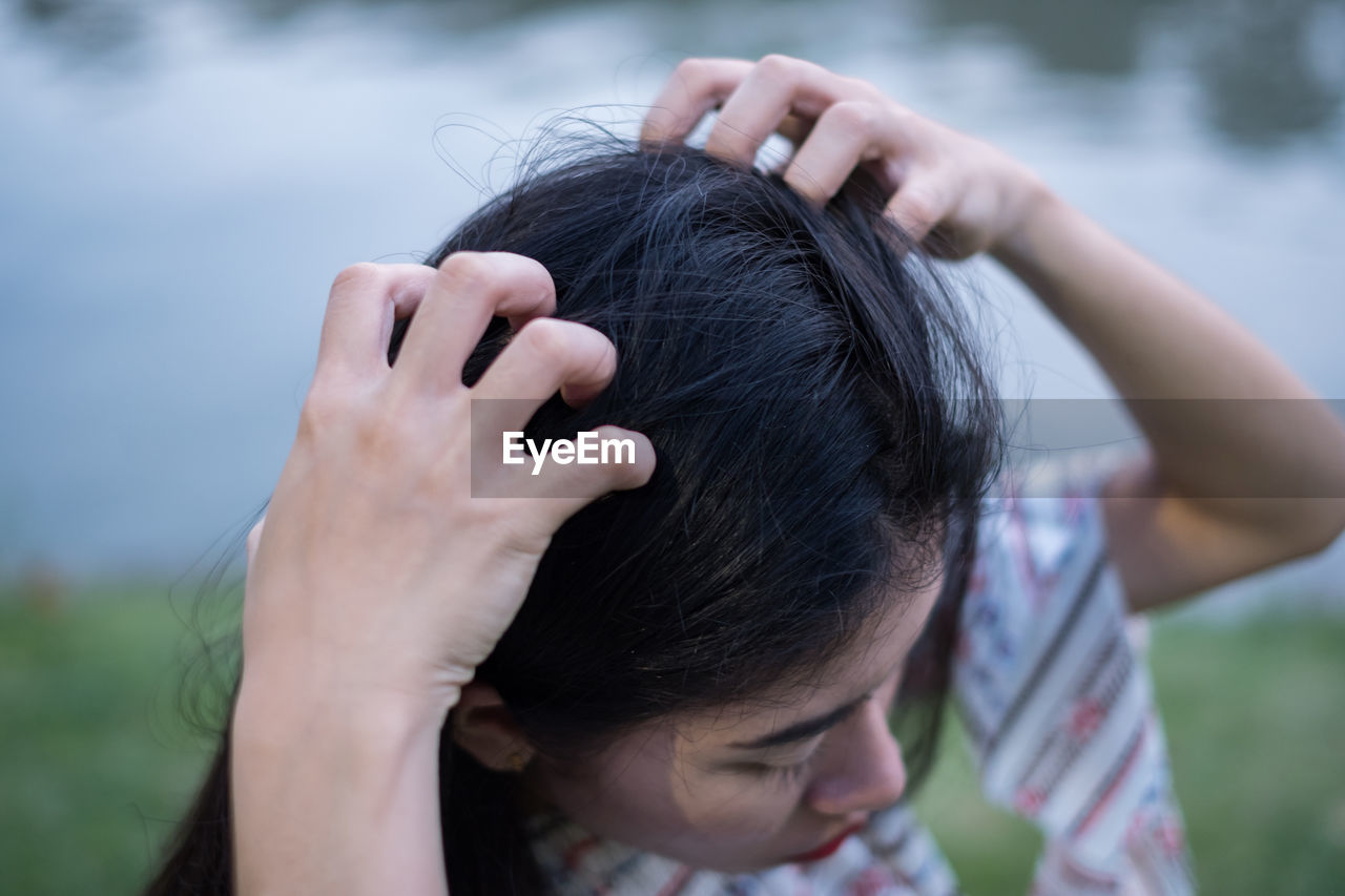 Close-up of woman scratching head by lake in park