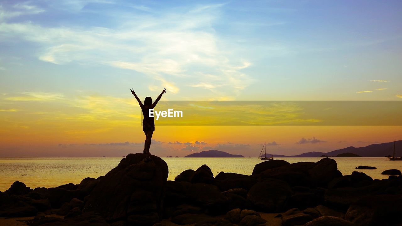 Silhouette woman on rock by sea against sky during sunset