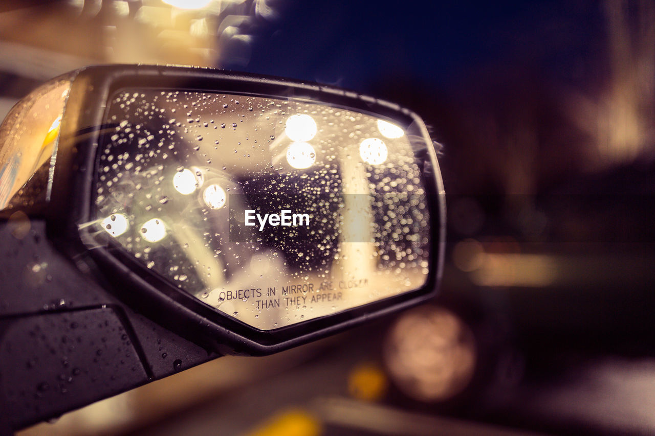 Cropped image of wet side-view mirror of car at night