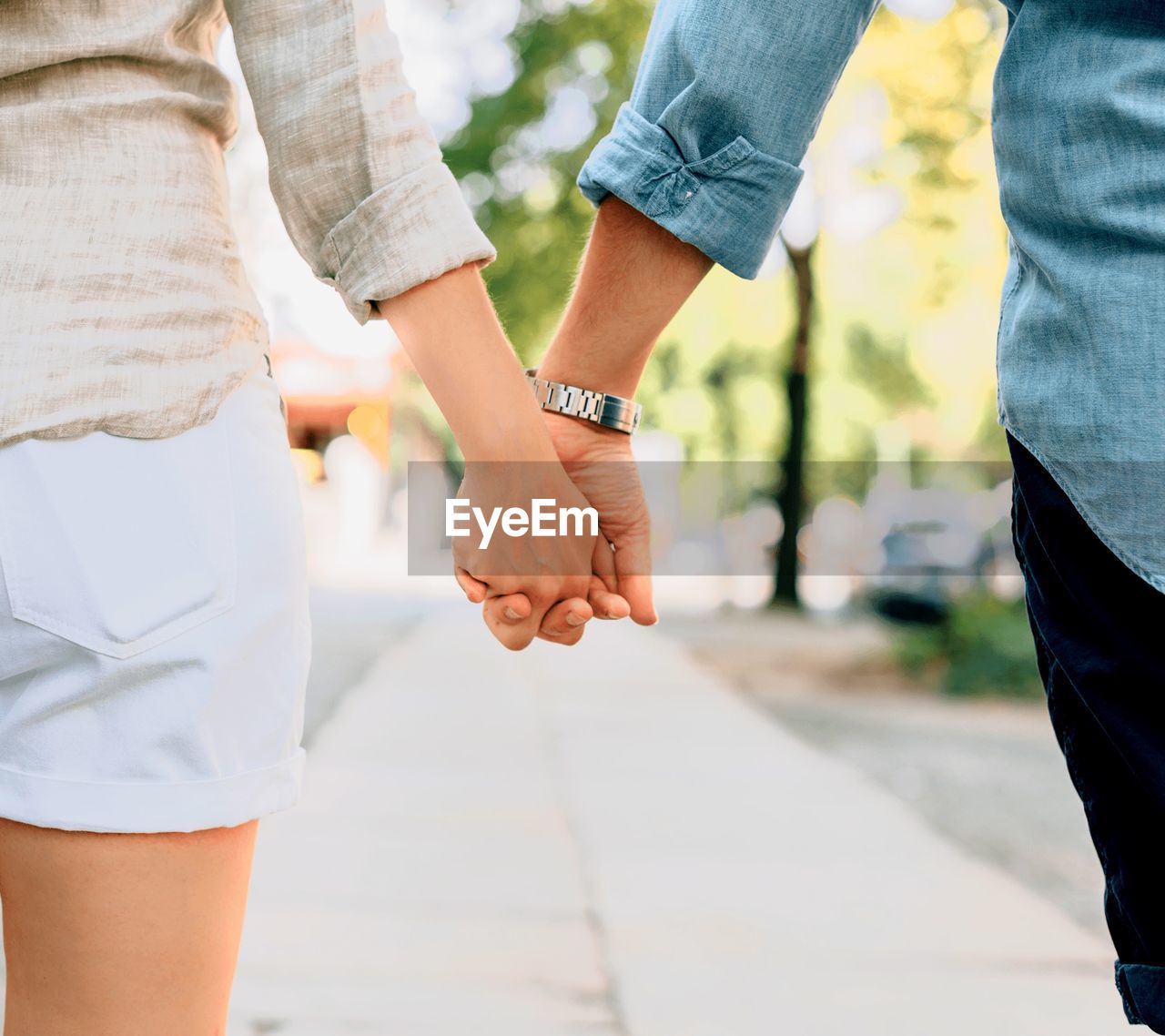 MIDSECTION OF COUPLE HOLDING HANDS OUTDOORS