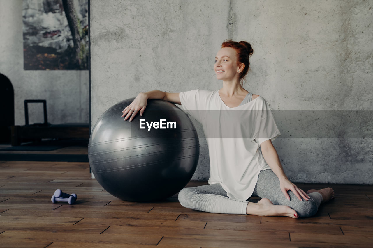 Smiling woman sitting by fitness ball at gym