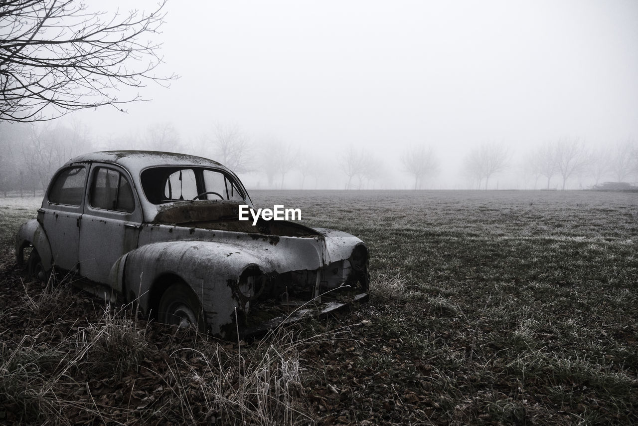 Abandoned car on field against clear sky