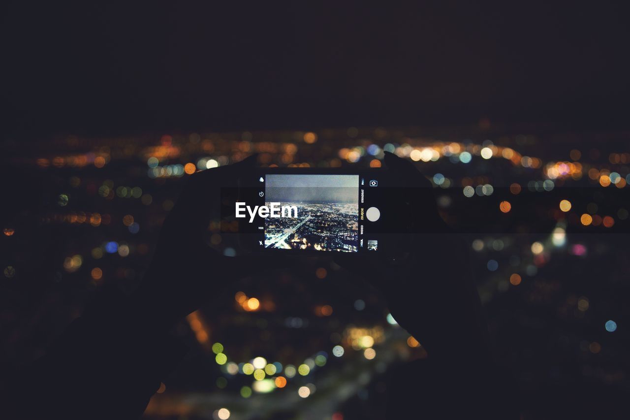 Cropped hands photographing illuminated cityscape at night