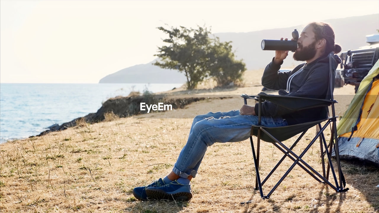 MAN PHOTOGRAPHING WHILE SITTING ON SEAT AT BEACH