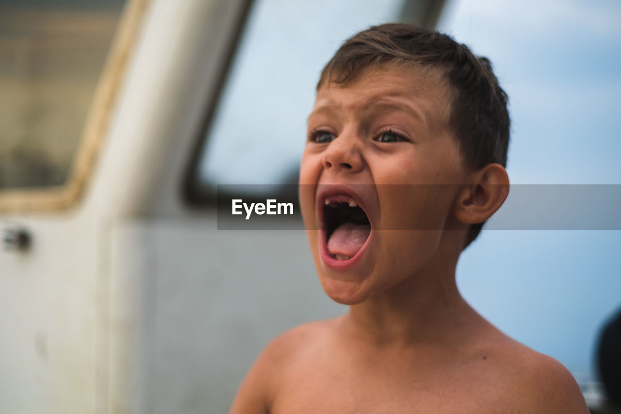 Close-up of shirtless boy screaming while standing at beach