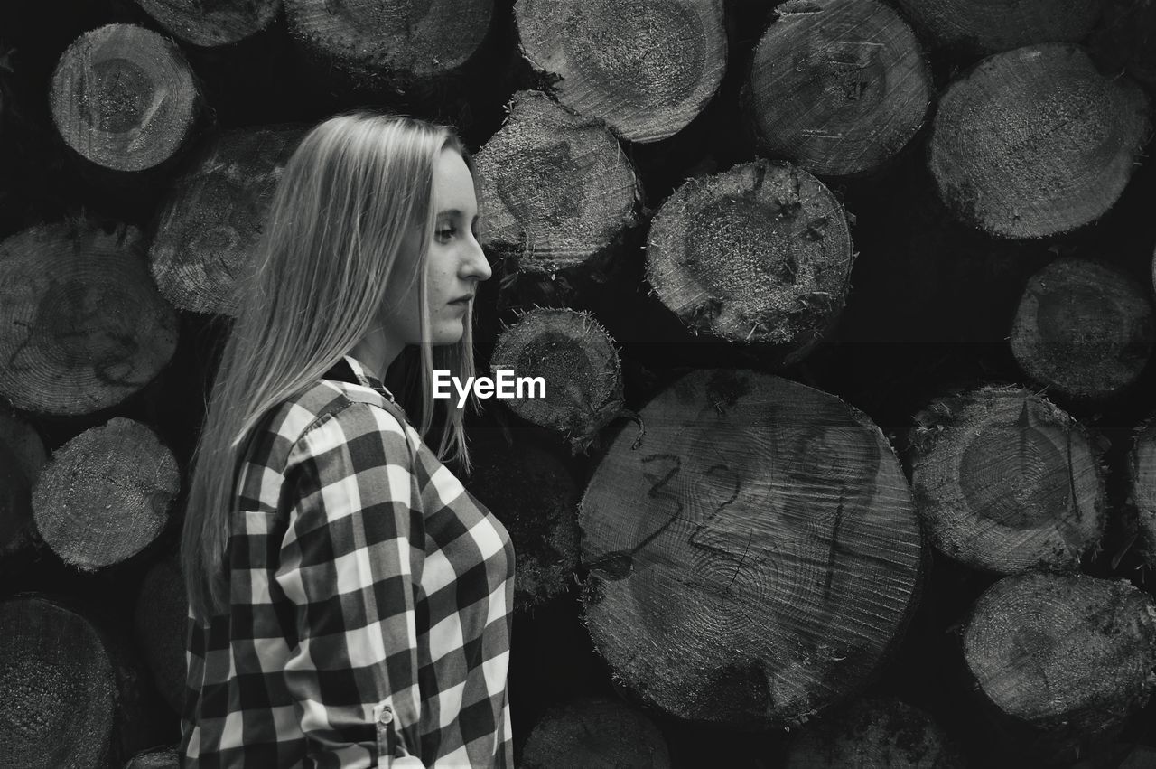 Side view of thoughtful woman standing against logs