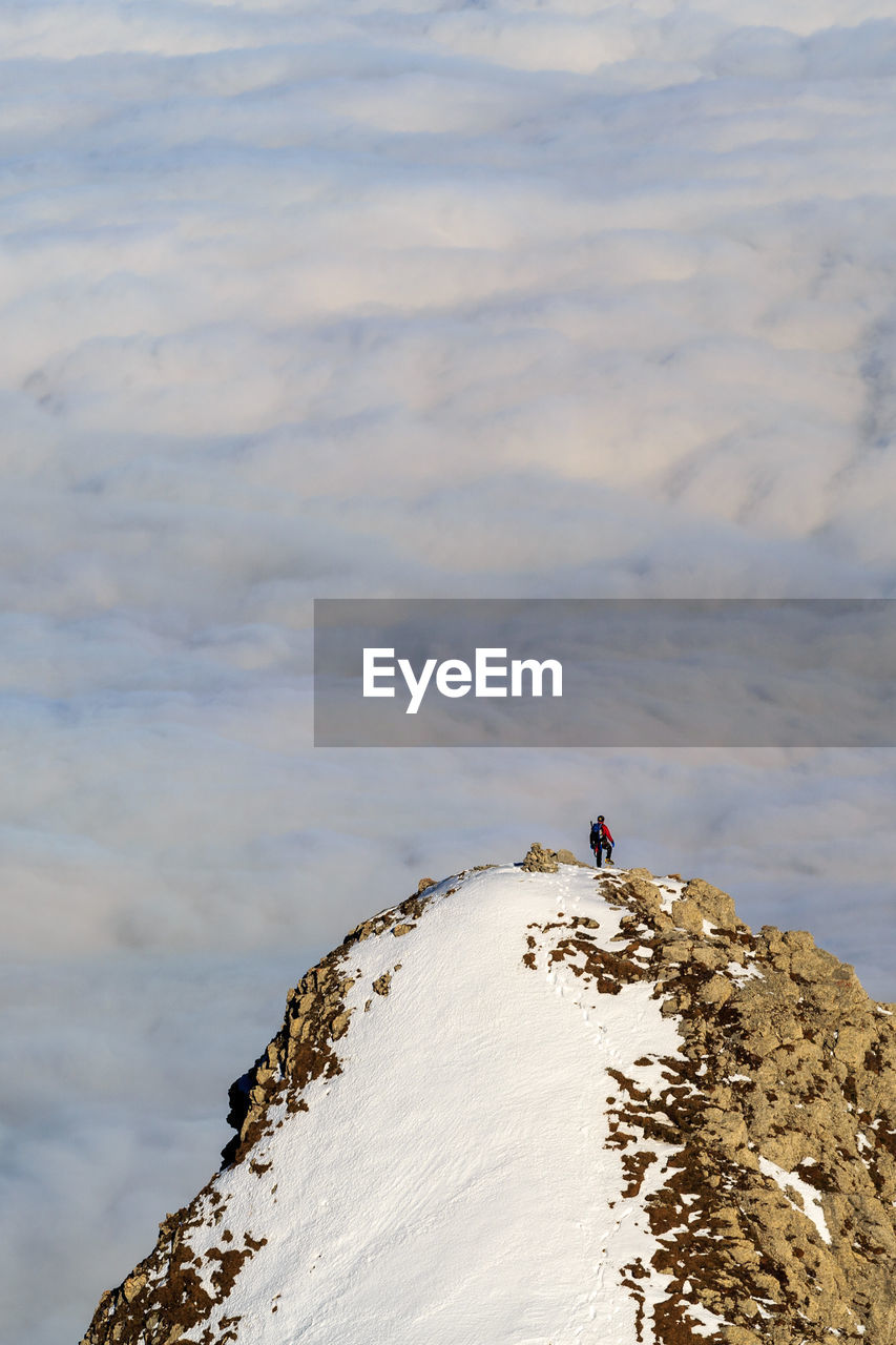 Rear view of man standing on rock against cloudy sky