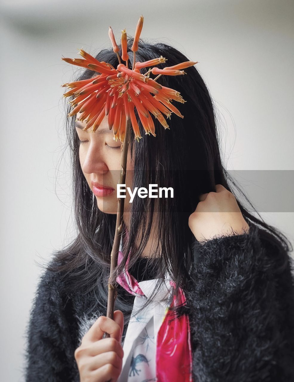 Close-up of woman holding stalk of orange aloe vera flower against white wall.