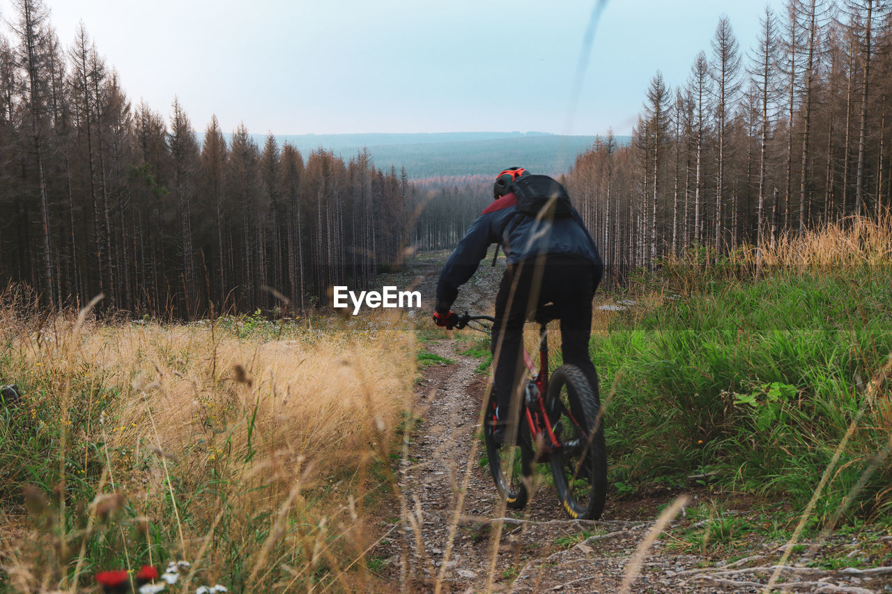 REAR VIEW OF SENIOR MAN RIDING BICYCLE ON FIELD