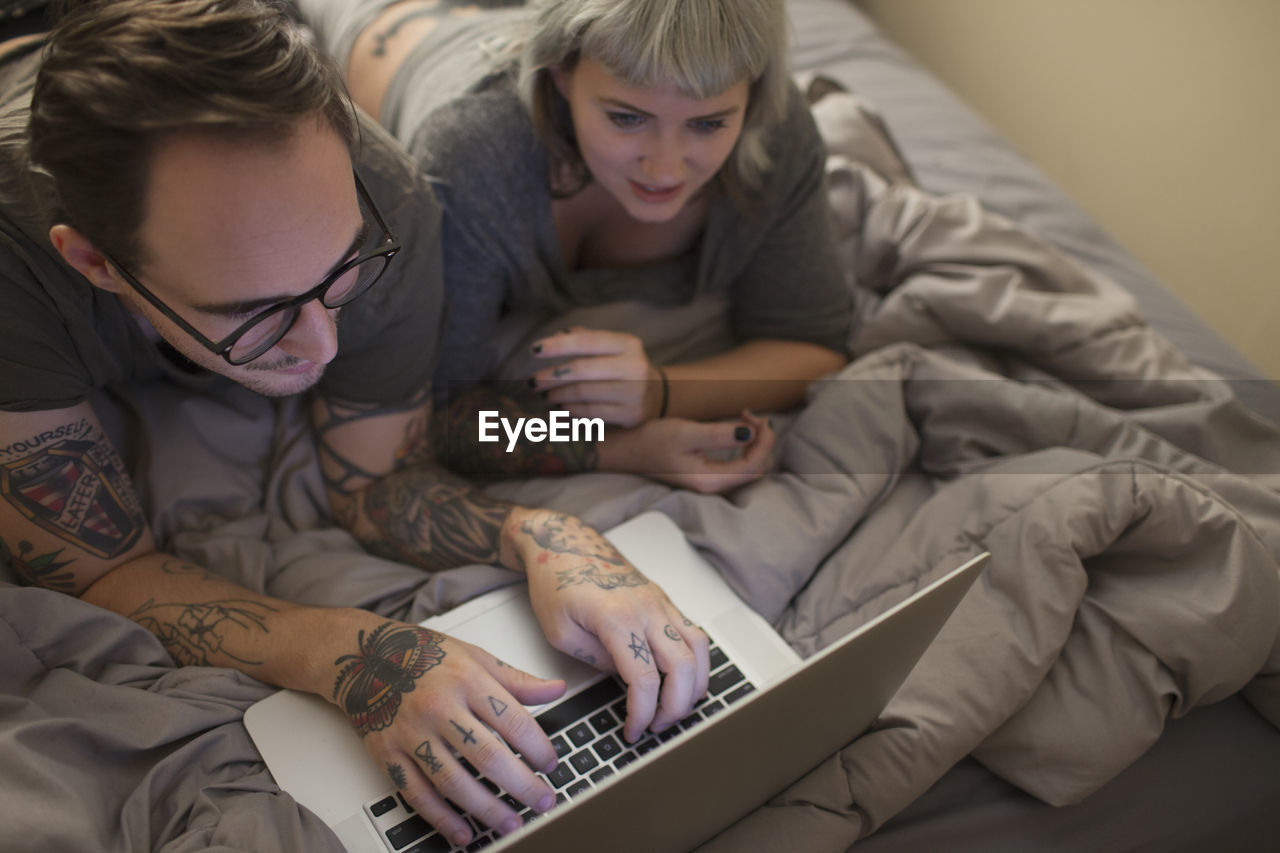 Young couple lying in bed looking at a laptop