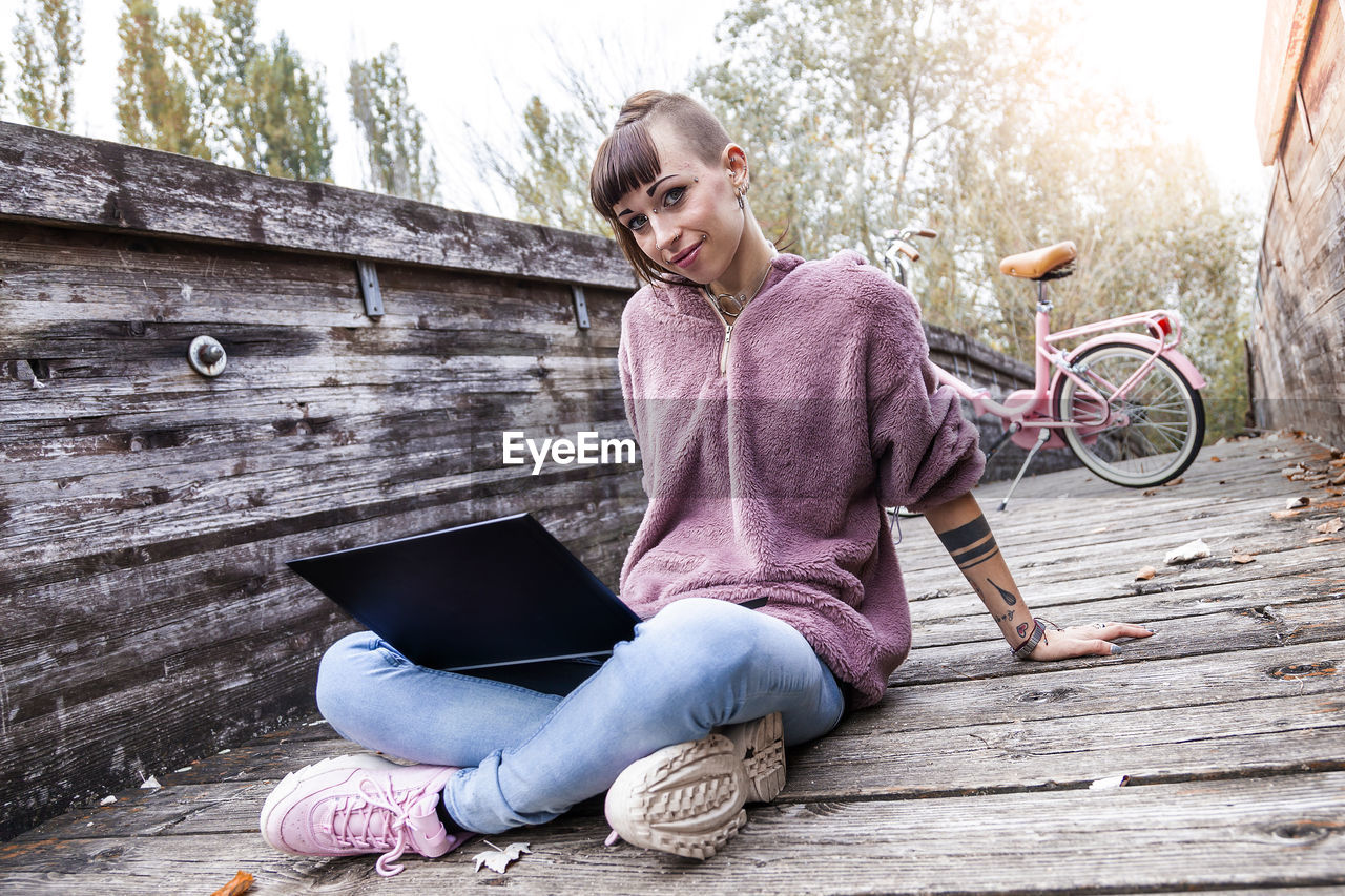 Portrait of young woman using laptop while sitting on footbridge