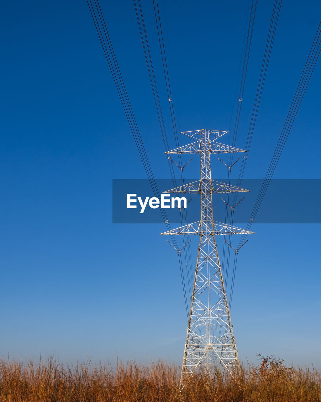 Electric pole and electric cable on the field in the countryside with blue sky.