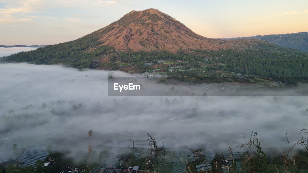 mountain, environment, landscape, wilderness, volcano, scenics - nature, nature, sky, fog, beauty in nature, land, travel destinations, morning, cloud, travel, water, plant, volcanic landscape, lake, smoke, mist, no people, tourism, mountain peak, geology, non-urban scene, outdoors, sunrise, tree, sun, tranquility, social issues, steam, mountain range, volcanic crater, twilight, grass, dawn, tranquil scene, plateau, activity, smog