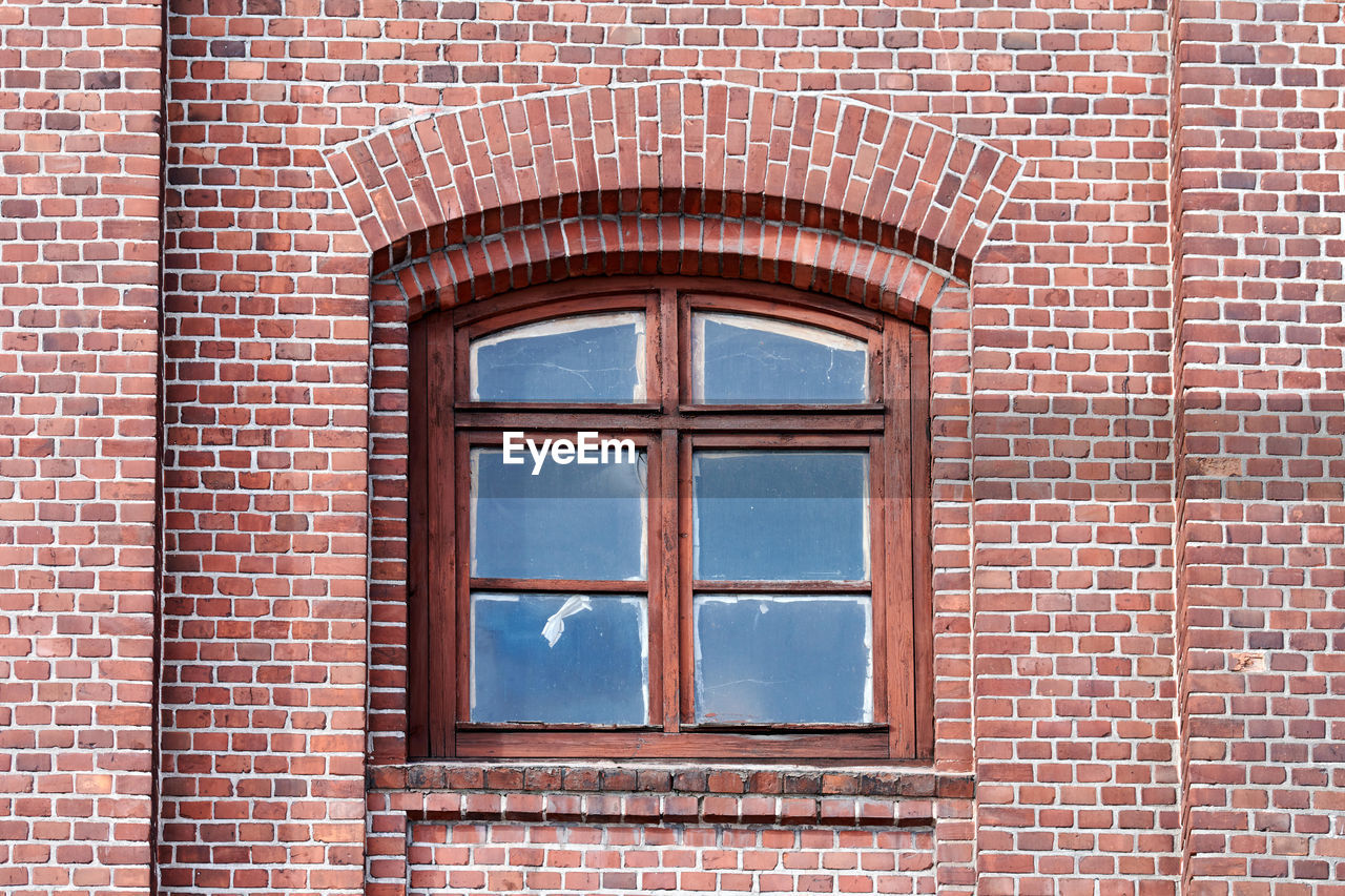 One arched glass window on old red brick wall. vintage window in brown wooden frame, red brick wall