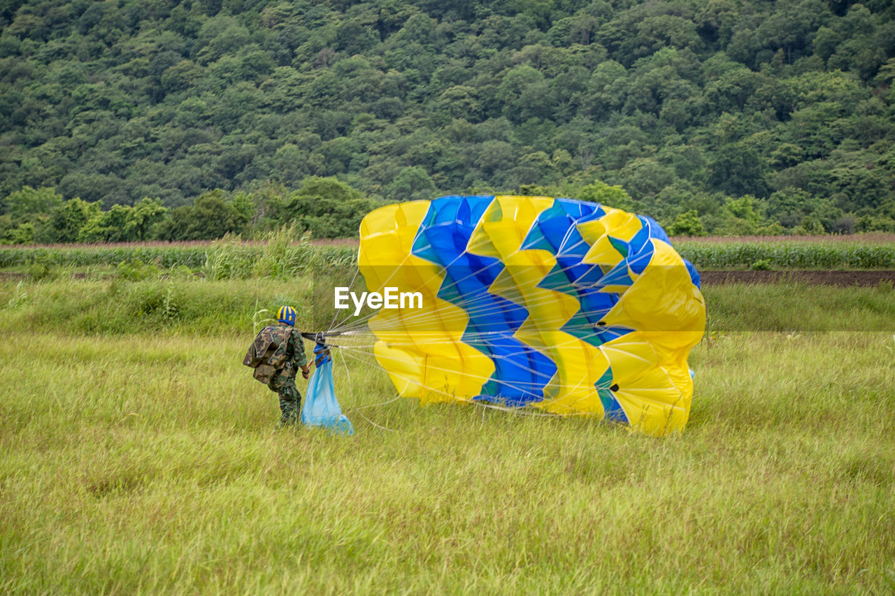 Army soldier with parachute walking on field against trees
