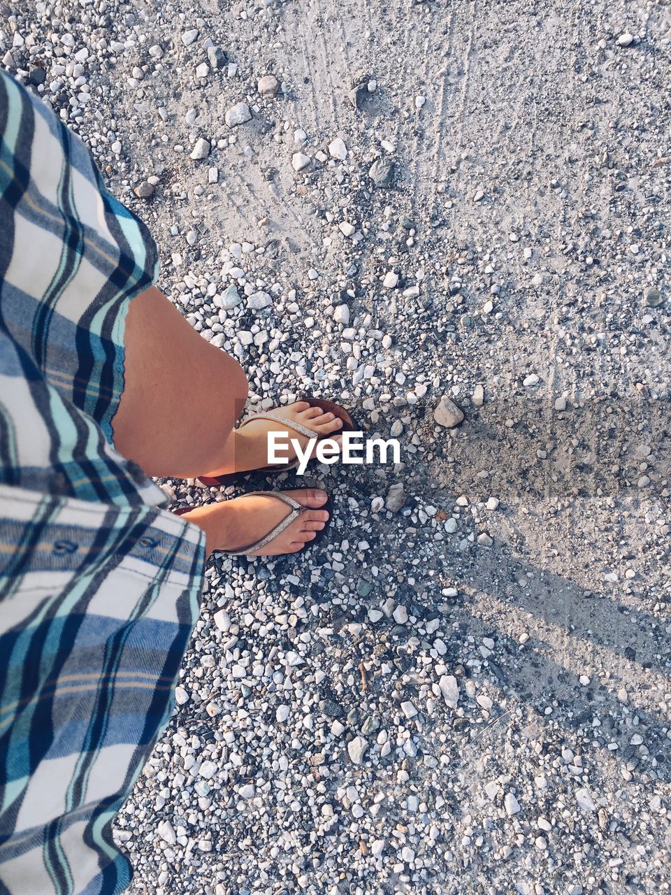 Cropped image of woman wearing checked shirt and t-shirts standing on pebbles