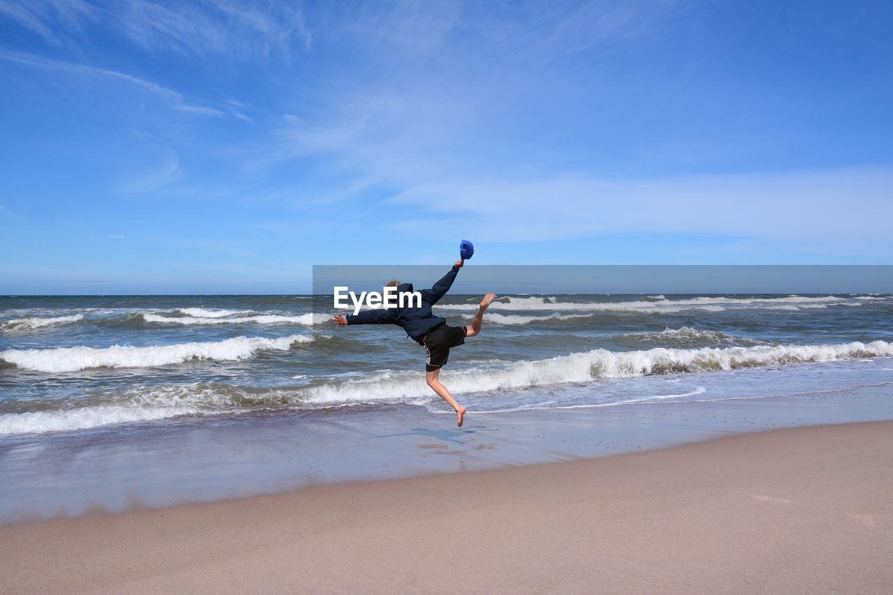 Rear view of playful man jumping on shore at beach