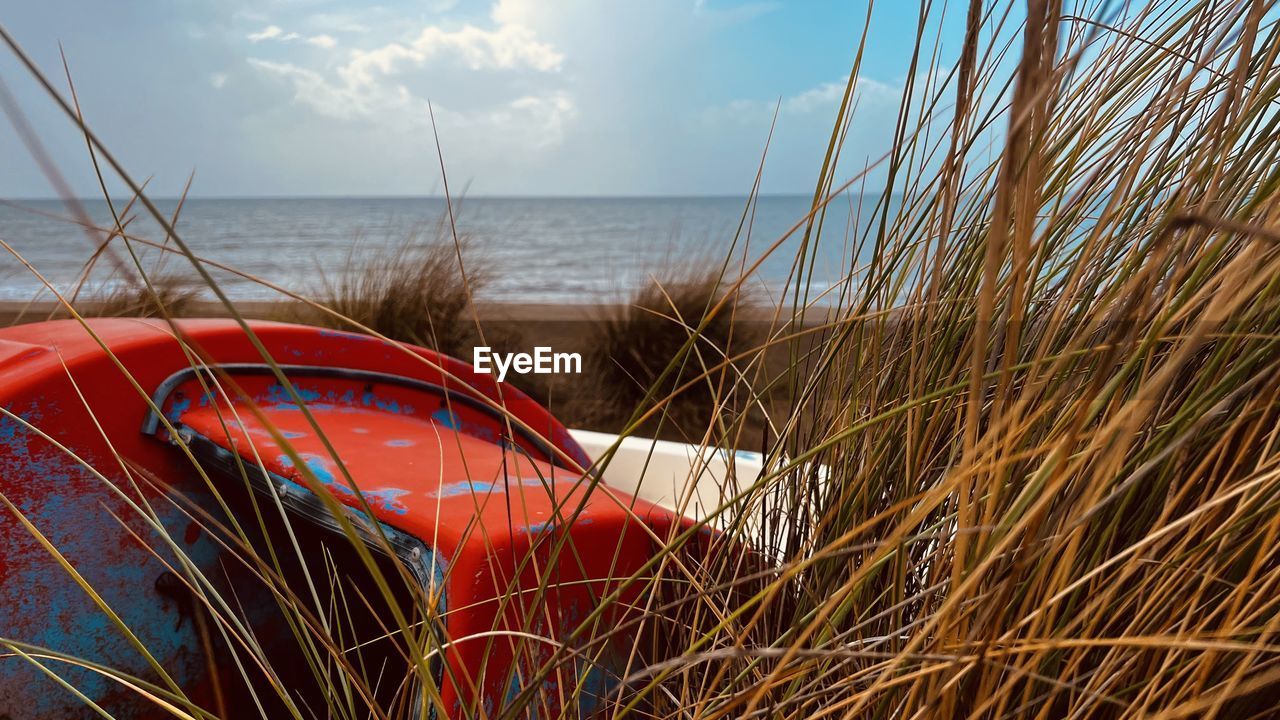 sea, water, sky, beach, nature, land, grass, plant, cloud, horizon over water, tranquility, horizon, no people, scenics - nature, beauty in nature, red, transportation, nautical vessel, day, shore, sand, mode of transportation, tranquil scene, outdoors, sunlight, coast, travel, marram grass, holiday, coastline, non-urban scene, vacation, trip, travel destinations, environment