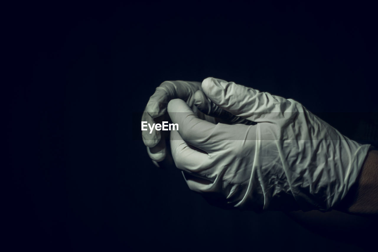 Cropped image of person wearing protective glove against black background