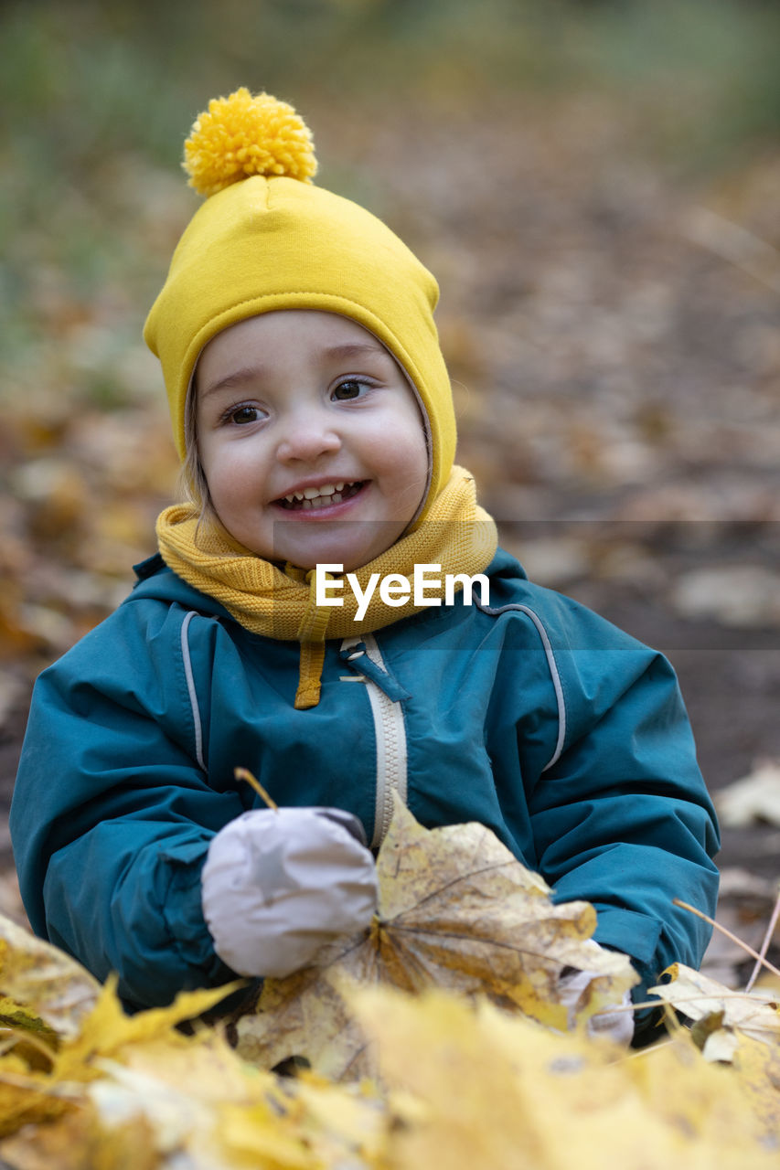 Little girl having fun autumn forest. kid sitting yellow leaves