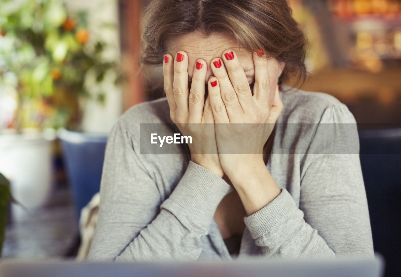 Sad young woman sitting with head in hands at home