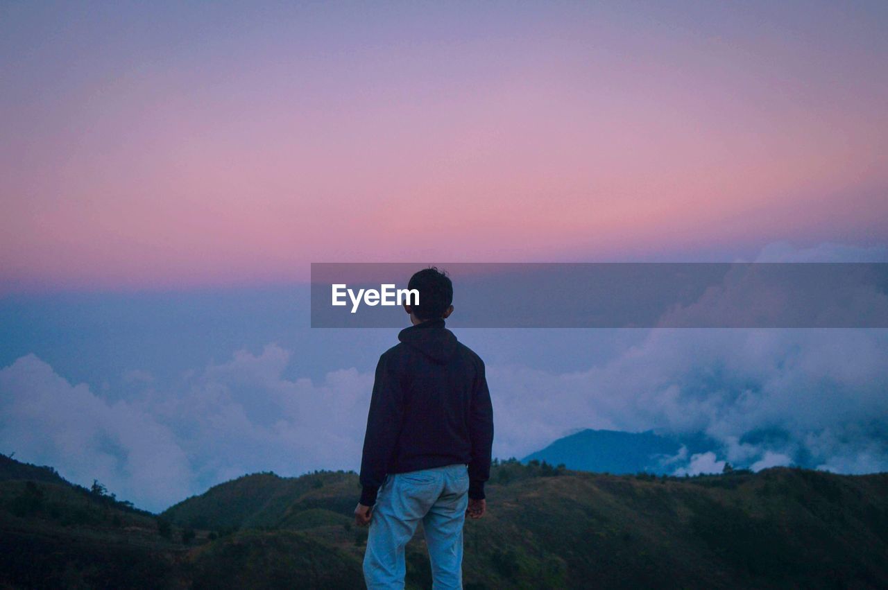 Rear view of man standing on mountain against sky