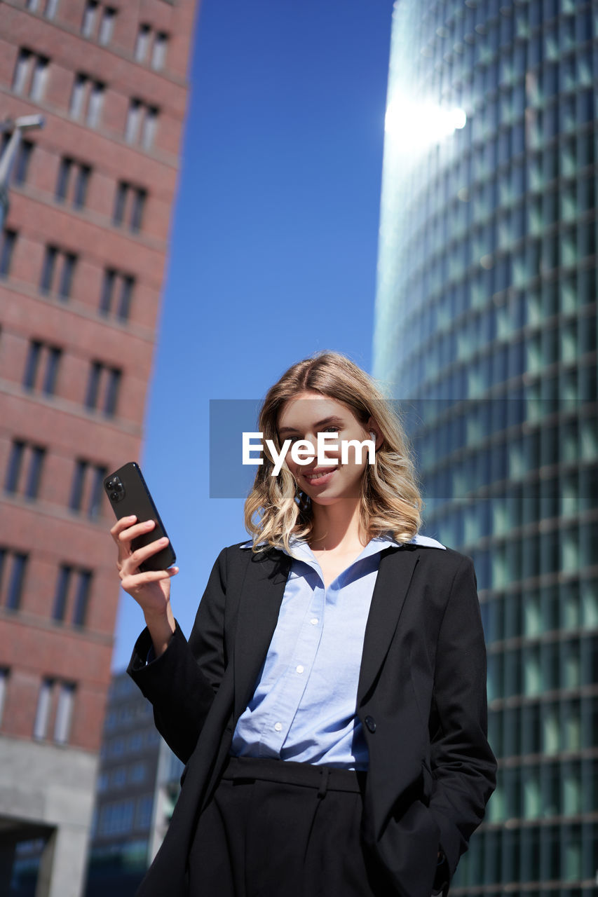 portrait of young woman using mobile phone while standing in city