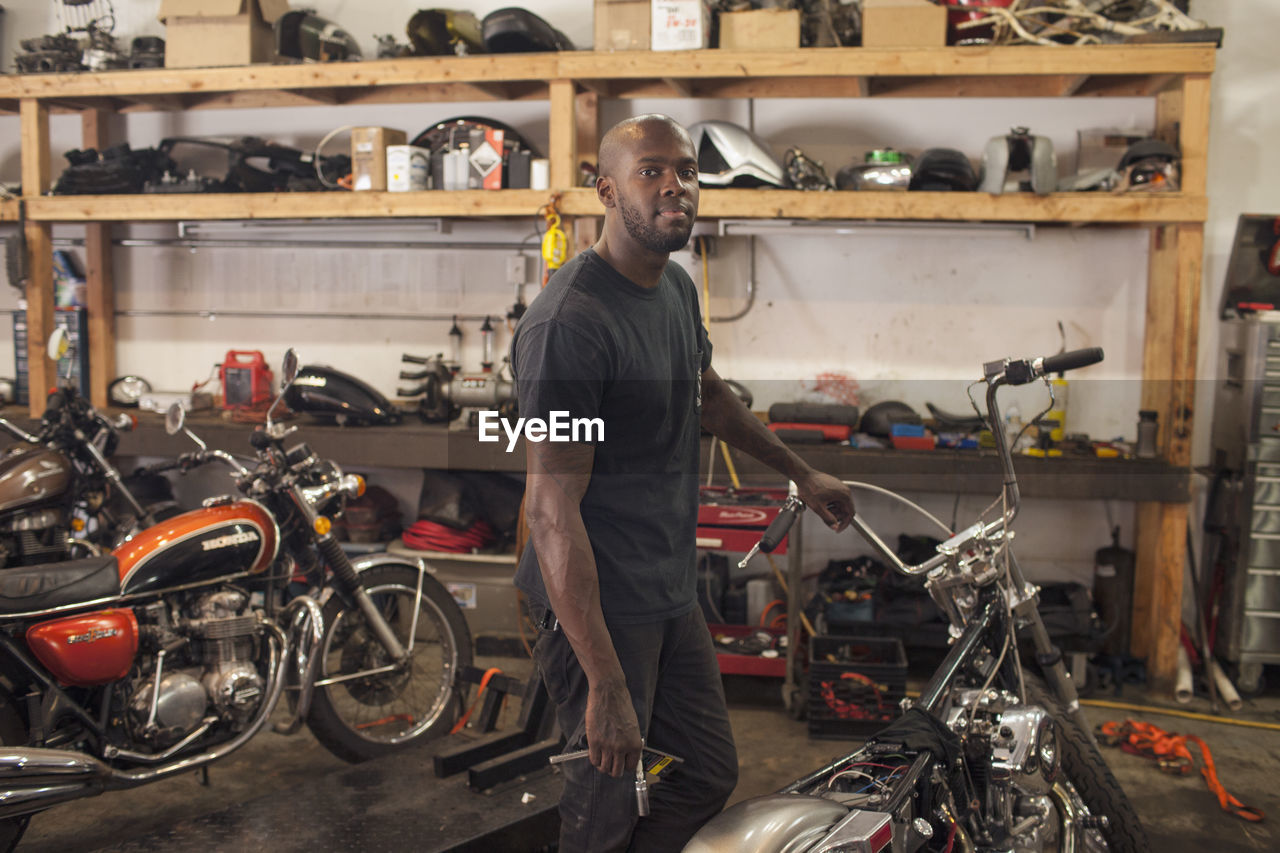 A young man in a garage with motorycles. 