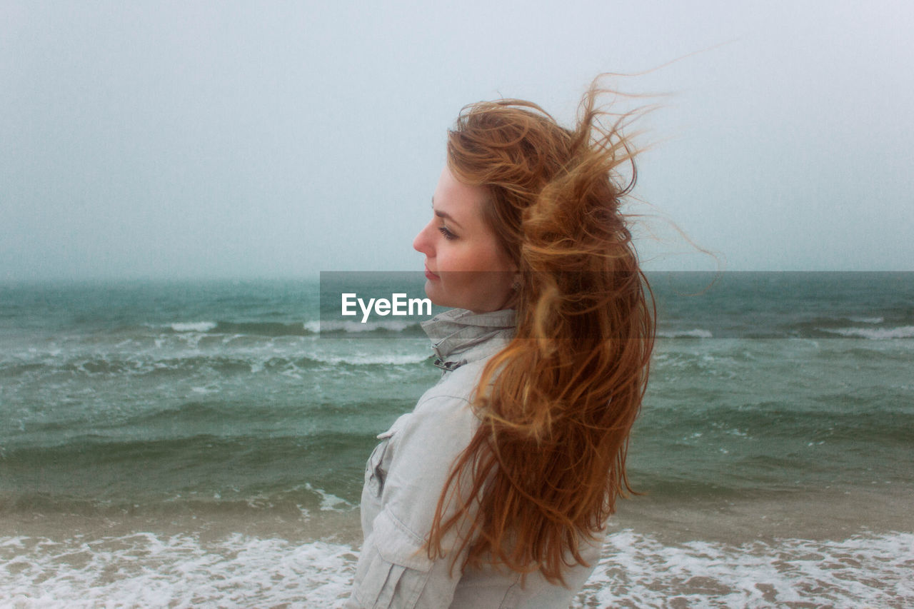 Beautiful woman standing at beach against sky