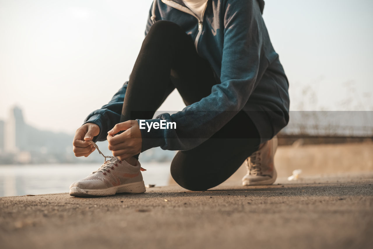 LOW SECTION OF WOMAN SITTING OUTDOORS AGAINST SKY