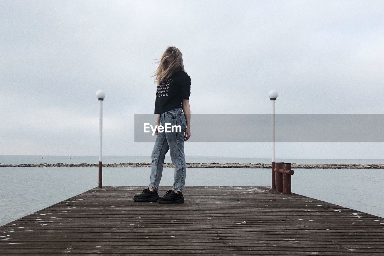 Rear view of woman standing on pier over sea against sky