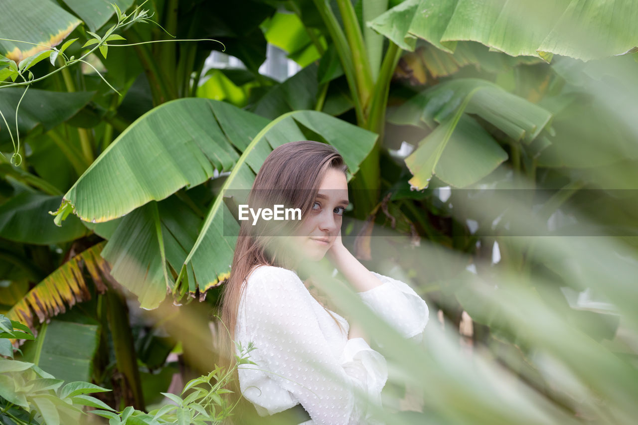 Portrait of young woman standing by banana leaf outdoors