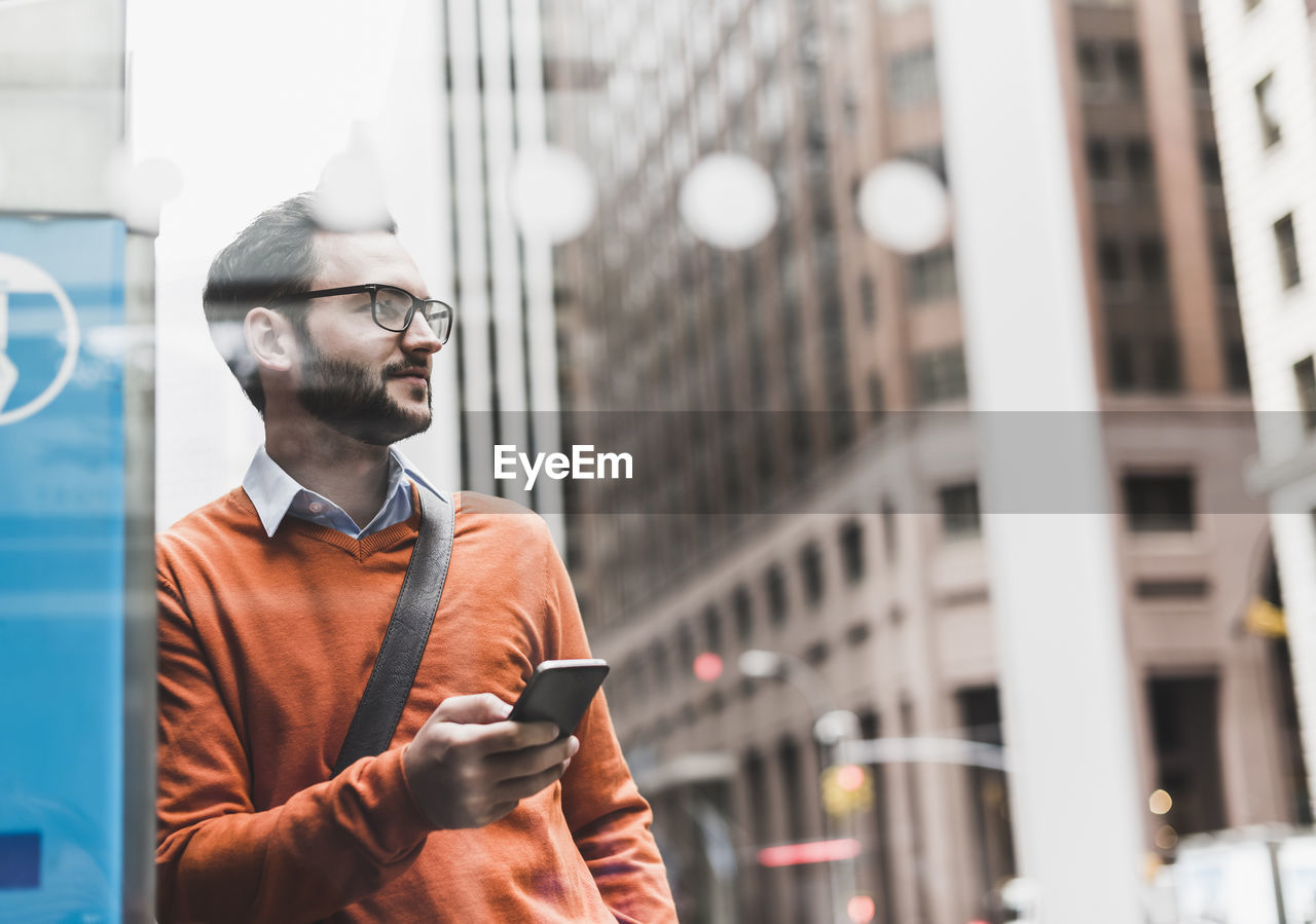 Usa, new york city, businessman leaning on atm holding smart phone